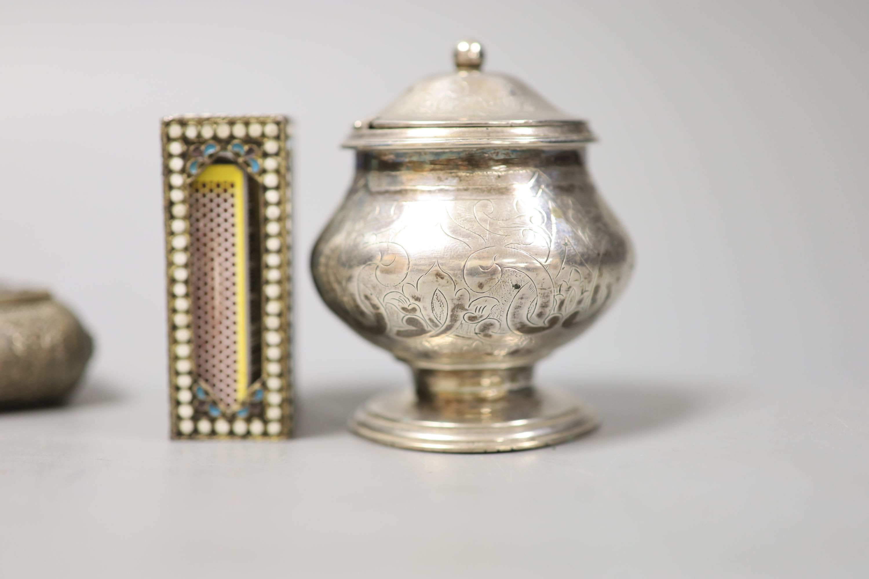 A filigree white metal cigarette box, an enamelled matchbox holder and a white metal mustard pot.